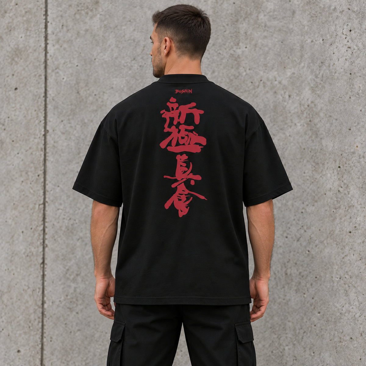Back view of a male model wearing a black BUSHIN oversized T-shirt with vertical crimson Shinkyokushin kanji and BUSHIN branding.