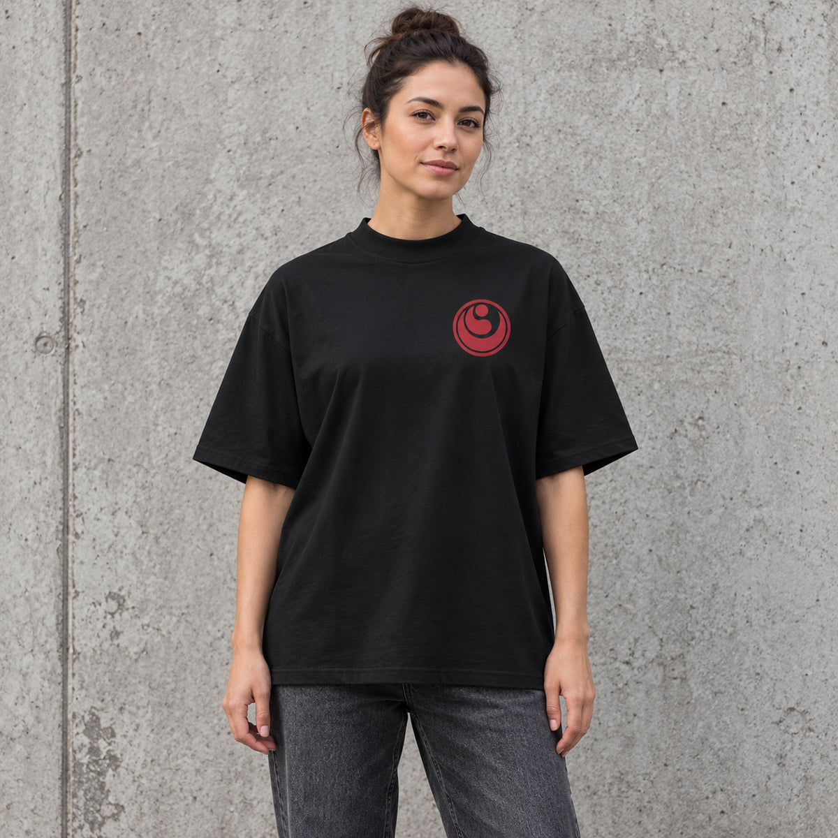 Female model wearing a black BUSHIN oversized high-neck T-shirt with a crimson Shinkyokushin chest emblem and charcoal jeans.
