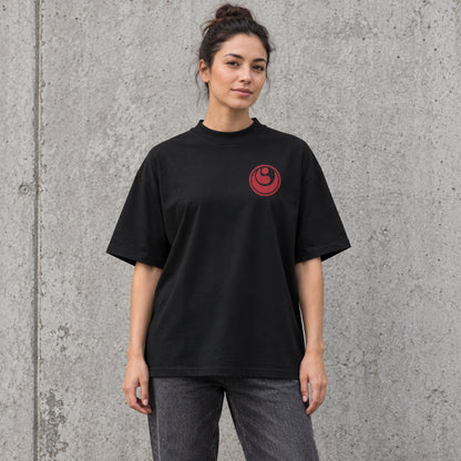 Female model wearing a black BUSHIN oversized high-neck T-shirt with a crimson Shinkyokushin chest emblem and charcoal jeans.
