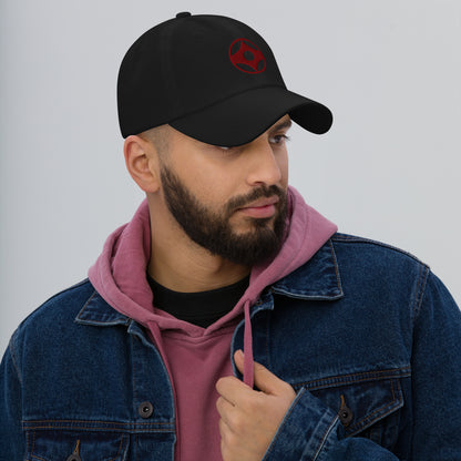 Man wearing a black cap with text, pink hoodie, and blue denim jacket on a gray background