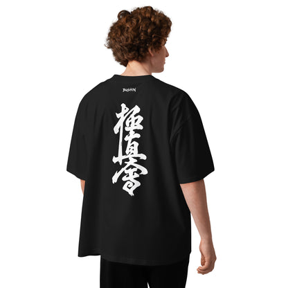 A person shown from the back wearing an oversized black T-shirt with large white Japanese calligraphy printed vertically on the back. The shirt has a small white brand wordmark near the neckline.