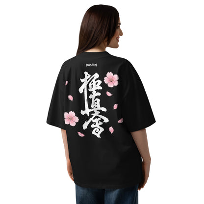 A woman shown from the back wearing an oversized black T-shirt with large white Japanese calligraphy and pink cherry blossom graphics on the back, photographed against a plain white studio background.