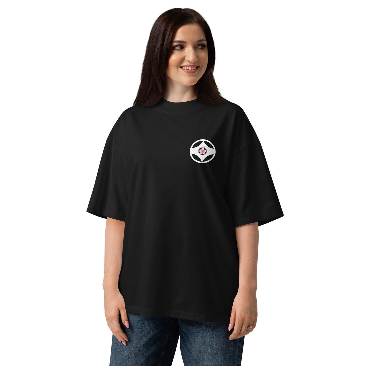 A woman modeling an oversized black t-shirt with a small circular white and red logo on the left chest, set against a plain white background.