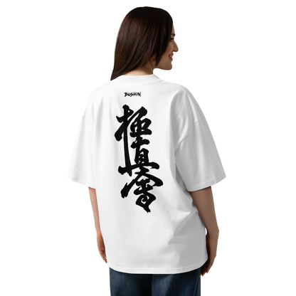 A woman shown from the back wearing an oversized white T-shirt with a large black Japanese kyokushin calligraphy graphic printed vertically on the back and a small 'BUSHIN' brand mark near the neckline.