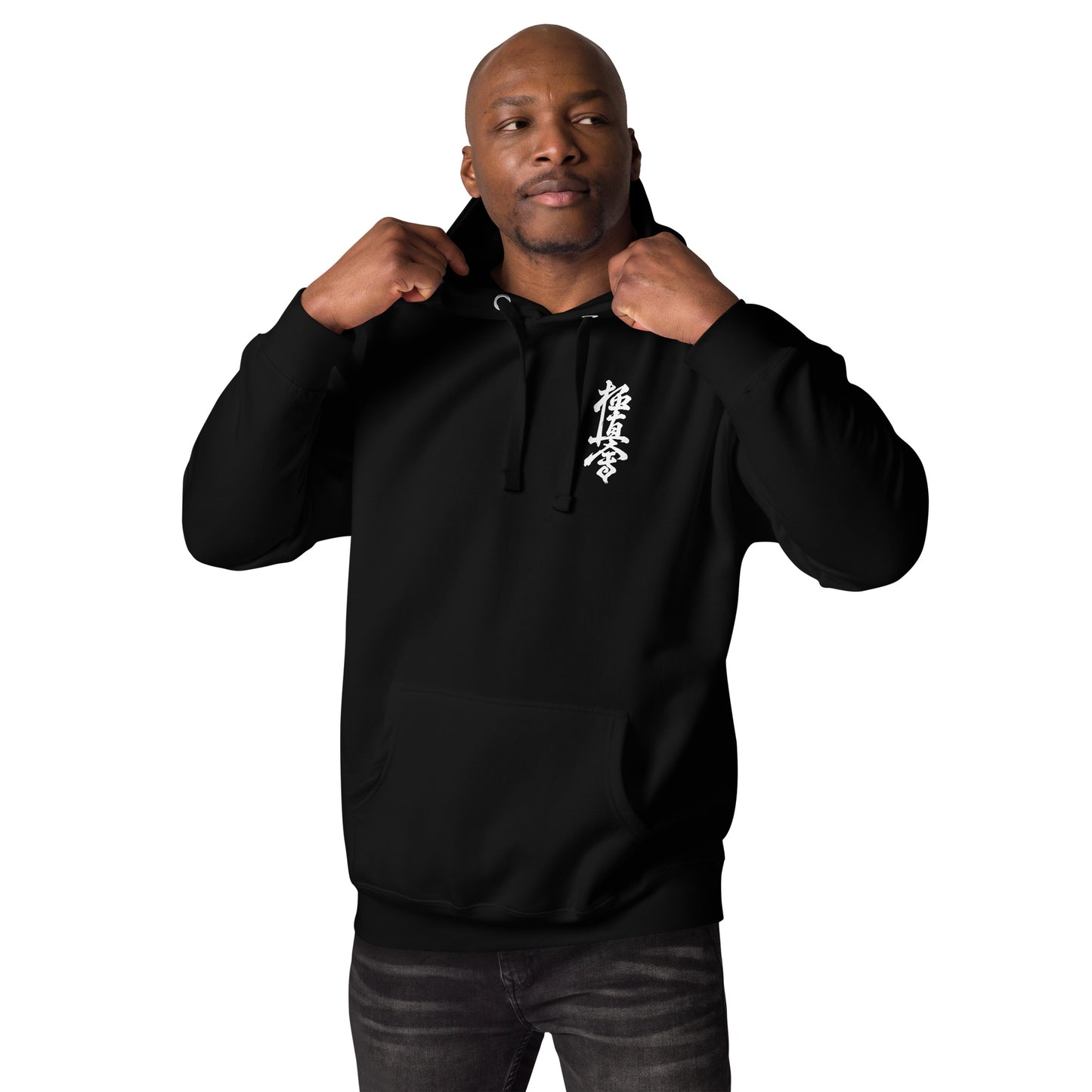 A man wearing a black pullover hoodie with a white vertical Japanese-style graphic on the left chest, posing with the hood up against a solid white background.