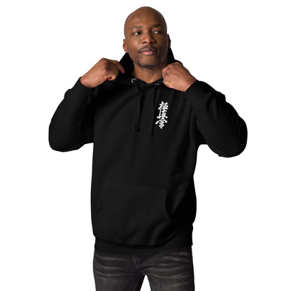 A man wearing a black pullover hoodie with a white vertical Japanese-style graphic on the left chest, posing with the hood up against a solid white background.