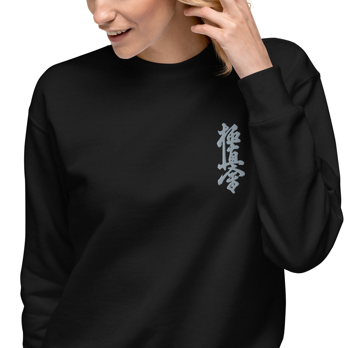 A woman wearing a black crewneck sweatshirt with a vertical white embroidered Kyokushin kanji on the left chest
