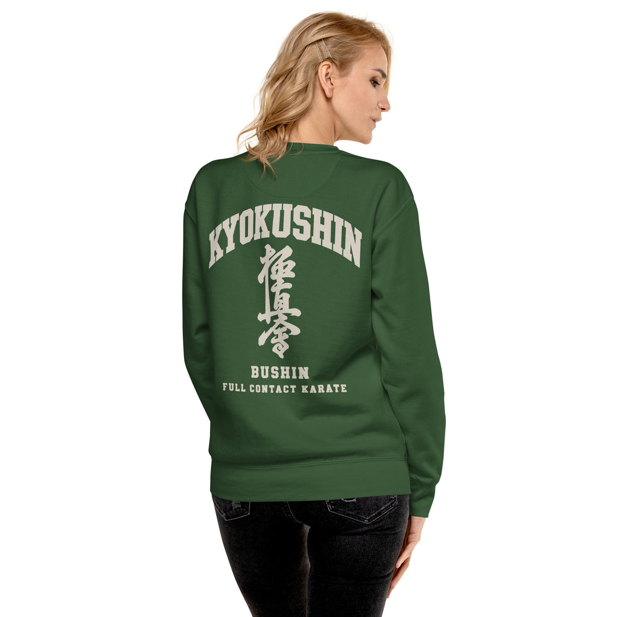 A woman shown from the back wearing a dark green crewneck sweatshirt with a large white graphic print on the back reading 'KYOKUSHIN BUSHIN FULL CONTACT KARATE' with Japanese characters. She is also wearing black jeans, set against a plain white background.